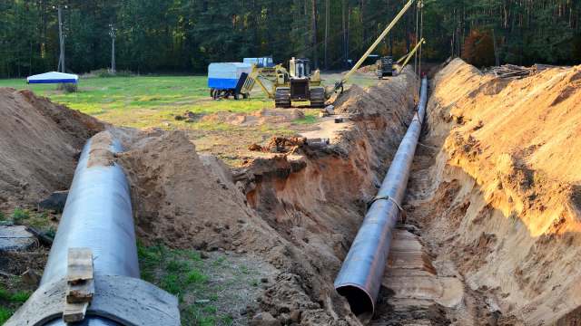A pipeline installation site with excavated earth and construction equipment nearby.