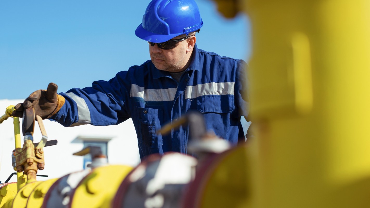 A worker in a blue uniform and helmet operates machinery on a sunny day.