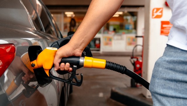 A person refuels a car at a gas station using an orange fuel nozzle.