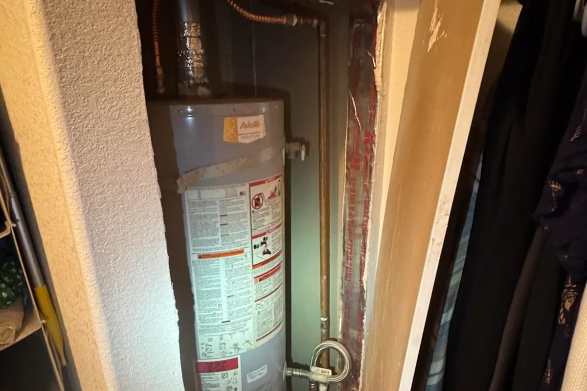 A water heater installed in a closet with copper piping and safety features.
