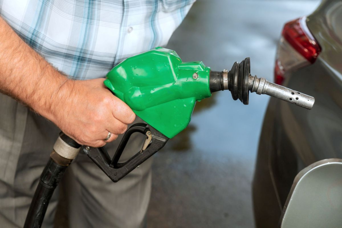 A person holding a green fuel pump nozzle near a vehicle.