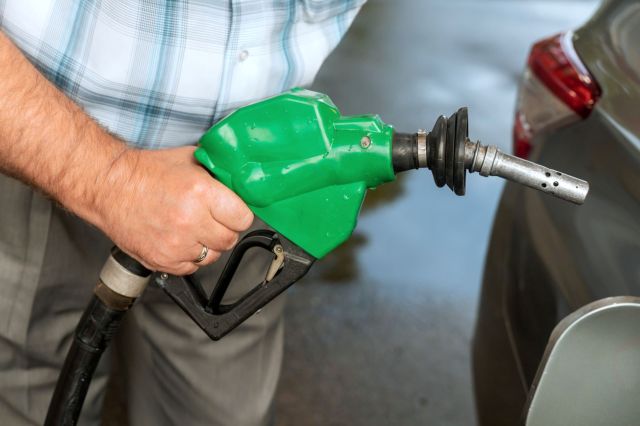 A person holding a green fuel pump nozzle near a vehicle.