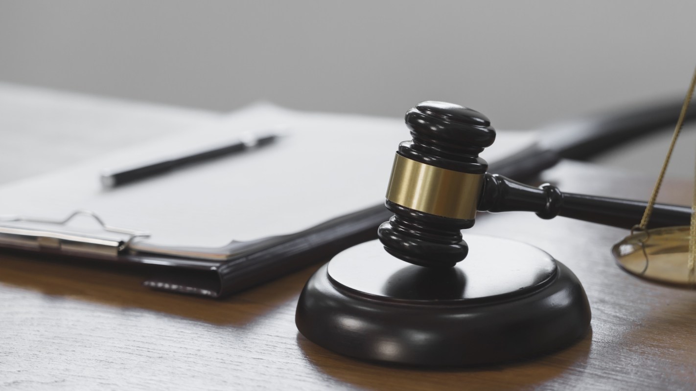 A gavel resting on a wooden desk next to a clipboard and pen.