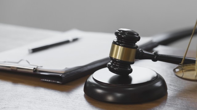 A gavel resting on a wooden desk next to a clipboard and pen.