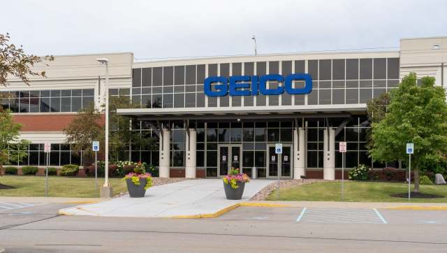 A GEICO office building with glass doors and flower planters in front.