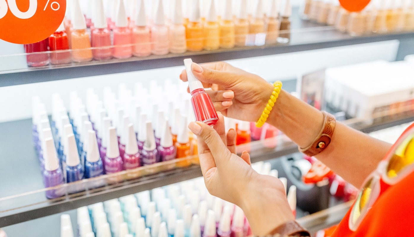 A person holds a bottle of red nail polish in a shop displaying various nail polish colors.