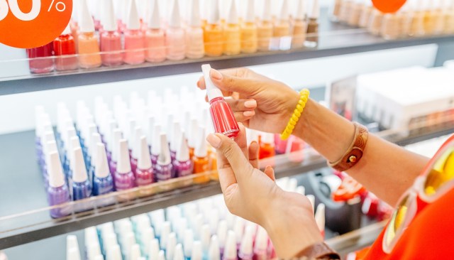 A person holds a bottle of red nail polish in a shop displaying various nail polish colors.