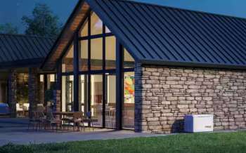A modern house with a stone exterior, large windows, and outdoor dining furniture in the yard.