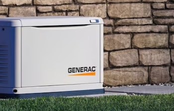 A Generac generator beside a stone wall on a grassy area.