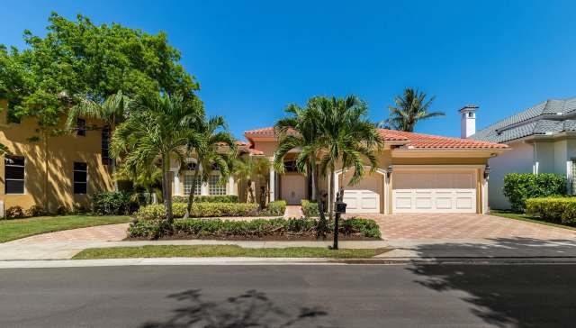 A residential home with a red tile roof, palm trees, and a landscaped yard.