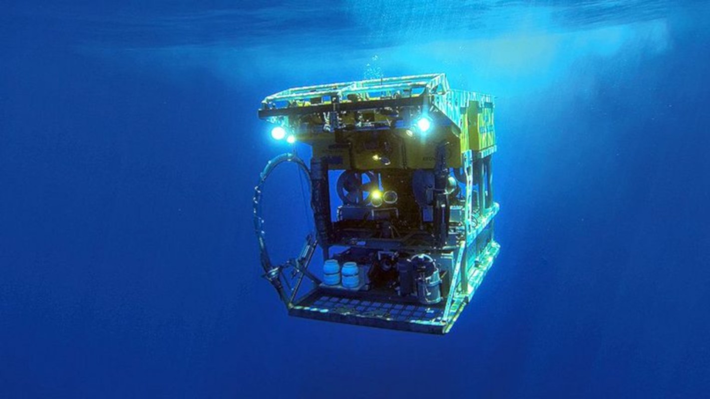 A submersible vehicle equipped with lights is navigating underwater in a blue environment.