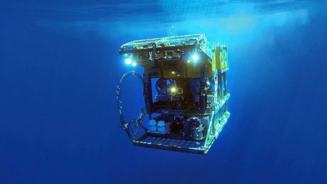 A submersible vehicle equipped with lights is navigating underwater in a blue environment.