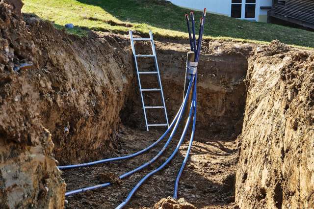 A trench with multiple blue pipes and a ladder nearby.
