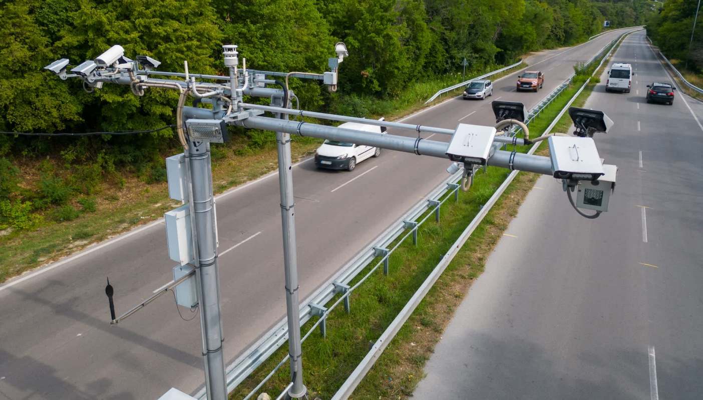 Traffic monitoring equipment is mounted above a road with vehicles passing by.