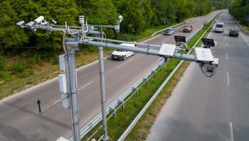 Traffic monitoring equipment is mounted above a road with vehicles passing by.
