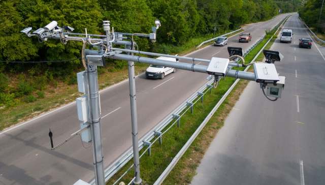 Traffic monitoring equipment is mounted above a road with vehicles passing by.