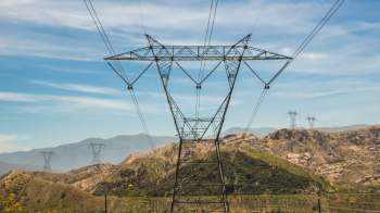 Power lines stretch across a mountainous landscape under a blue sky.