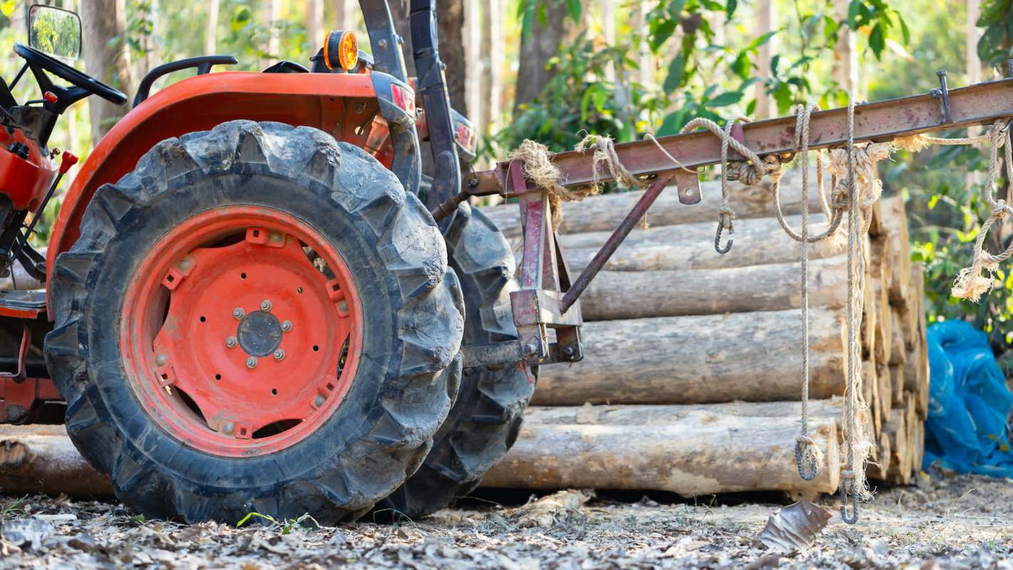 A tractor beside stacked logs.