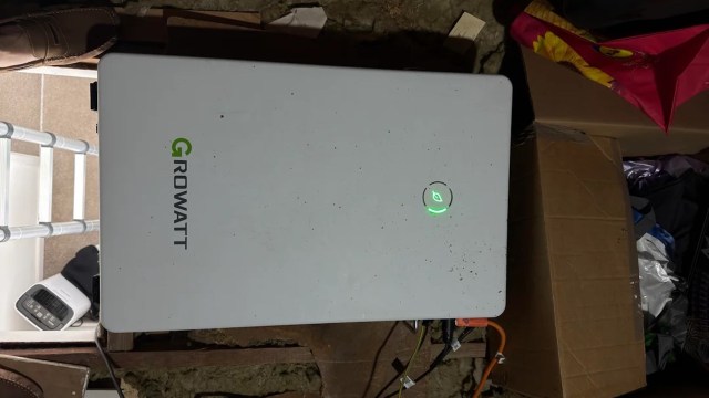 A power inverter with a green indicator light on a wooden surface among scattered items.