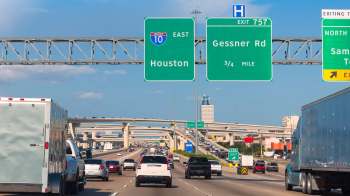 A busy highway with multiple lanes, exit signs, and vehicles, including trucks and cars.