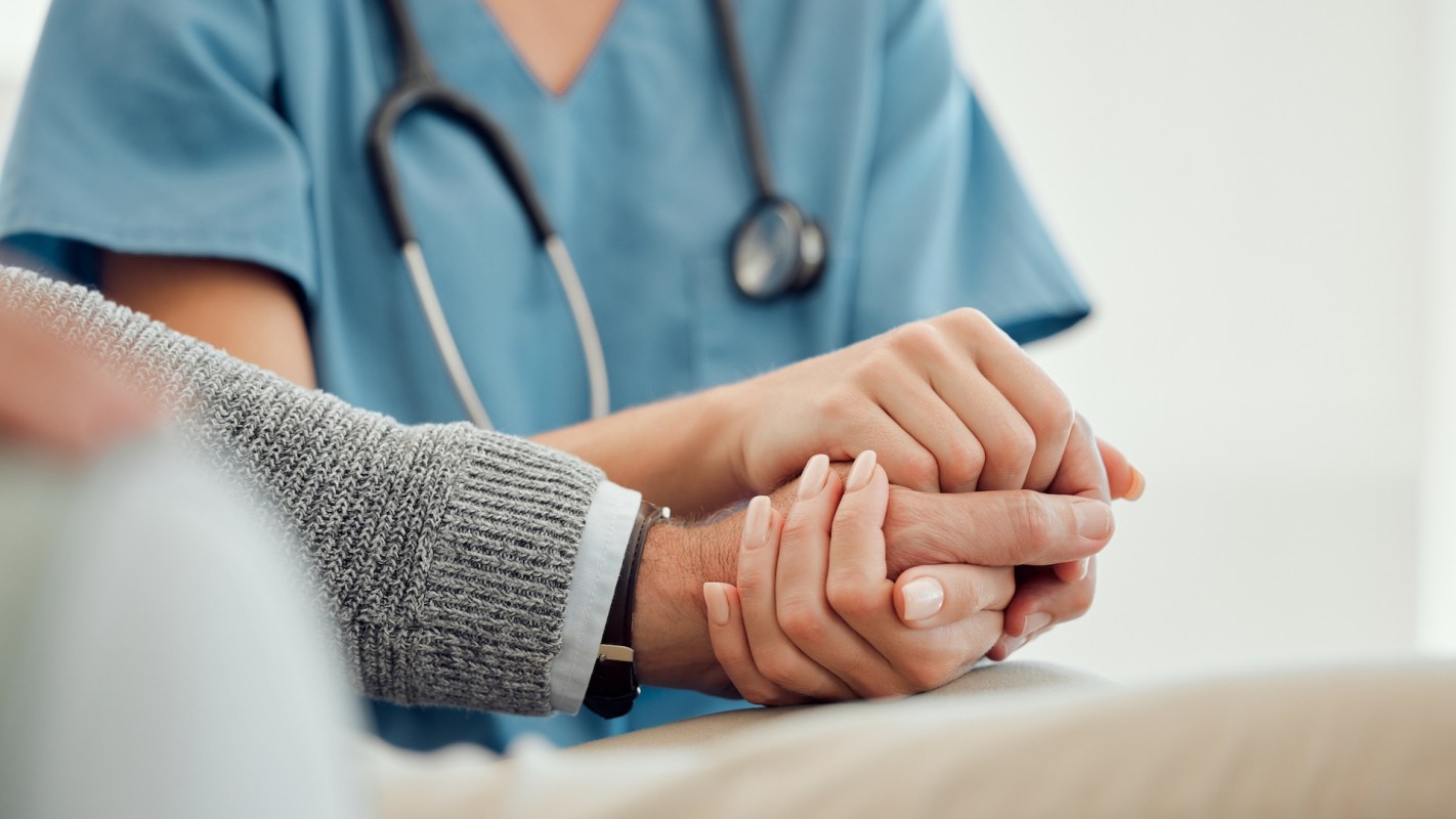 A healthcare professional and a patient hold hands in a medical setting.