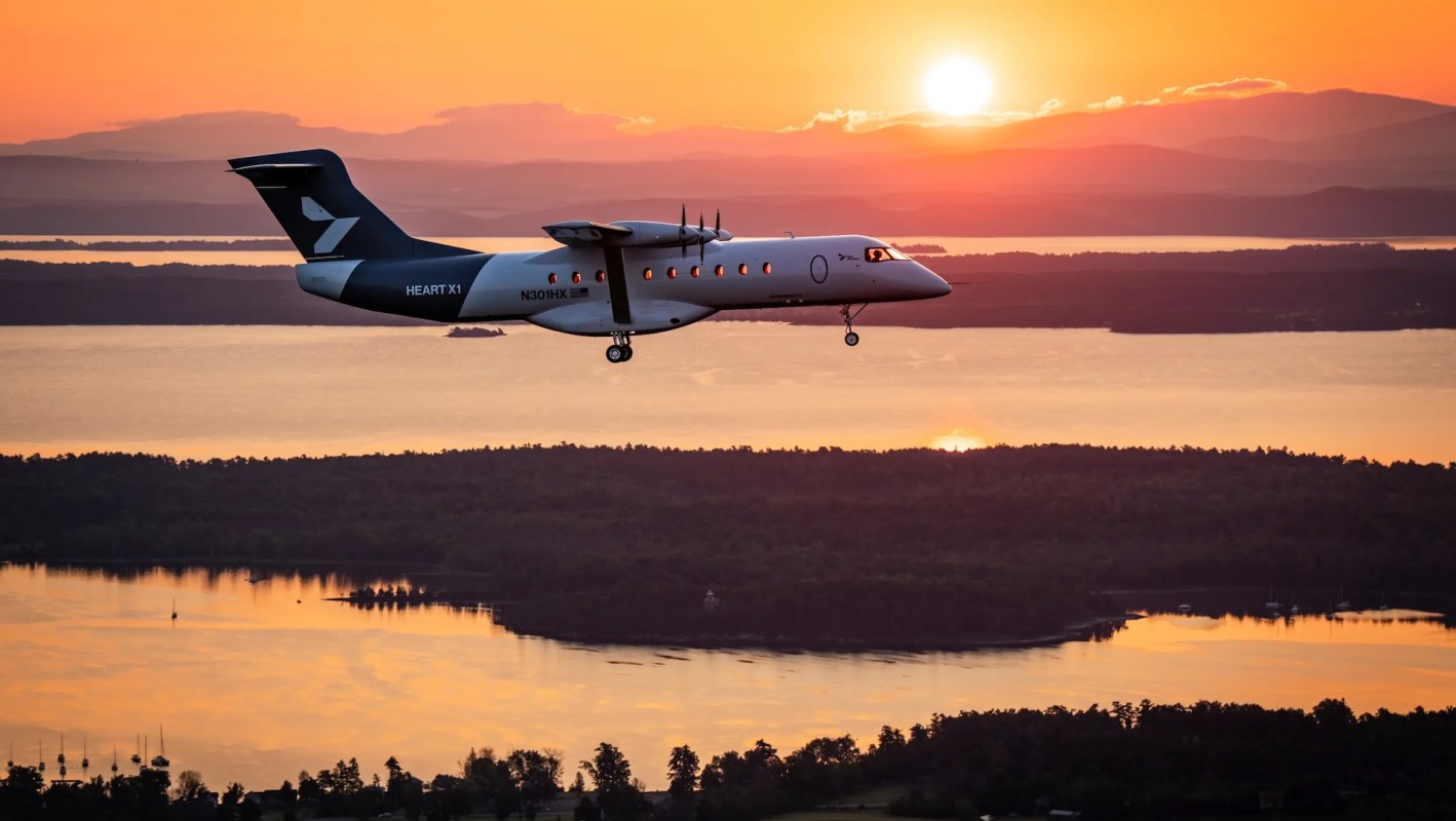 An aircraft flies over a body of water at sunset.