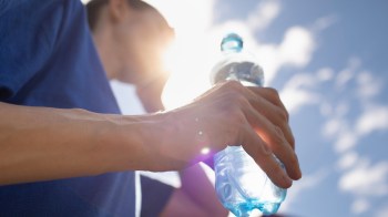 A person holds a water bottle while leaning against a railing under a bright sky.