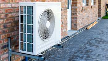 An outdoor air conditioning unit installed against a brick wall.