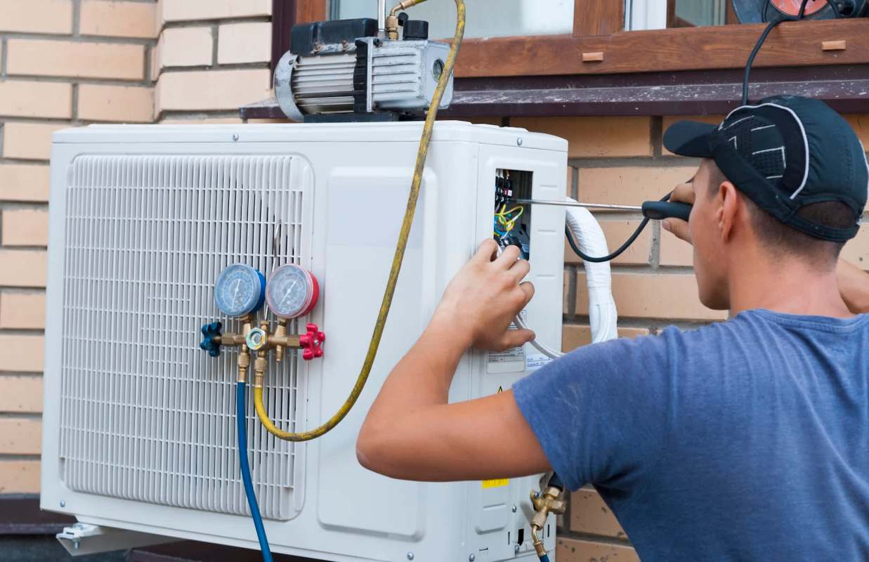 A technician installs a heat pump unit next to a wall.