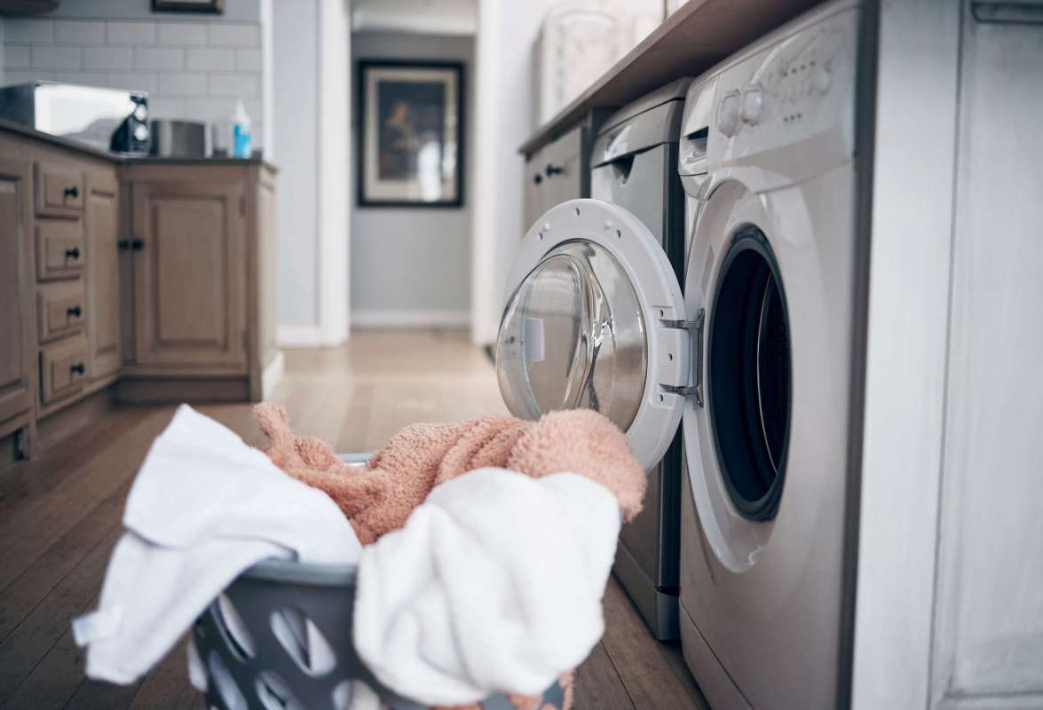 A laundry basket filled with towels in front of a washing machine in a kitchen setting.