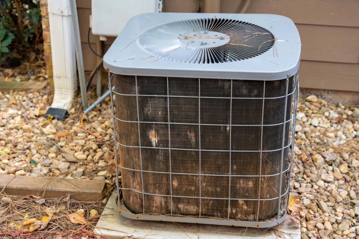 An outdoor air conditioning unit surrounded by gravel and vegetation.
