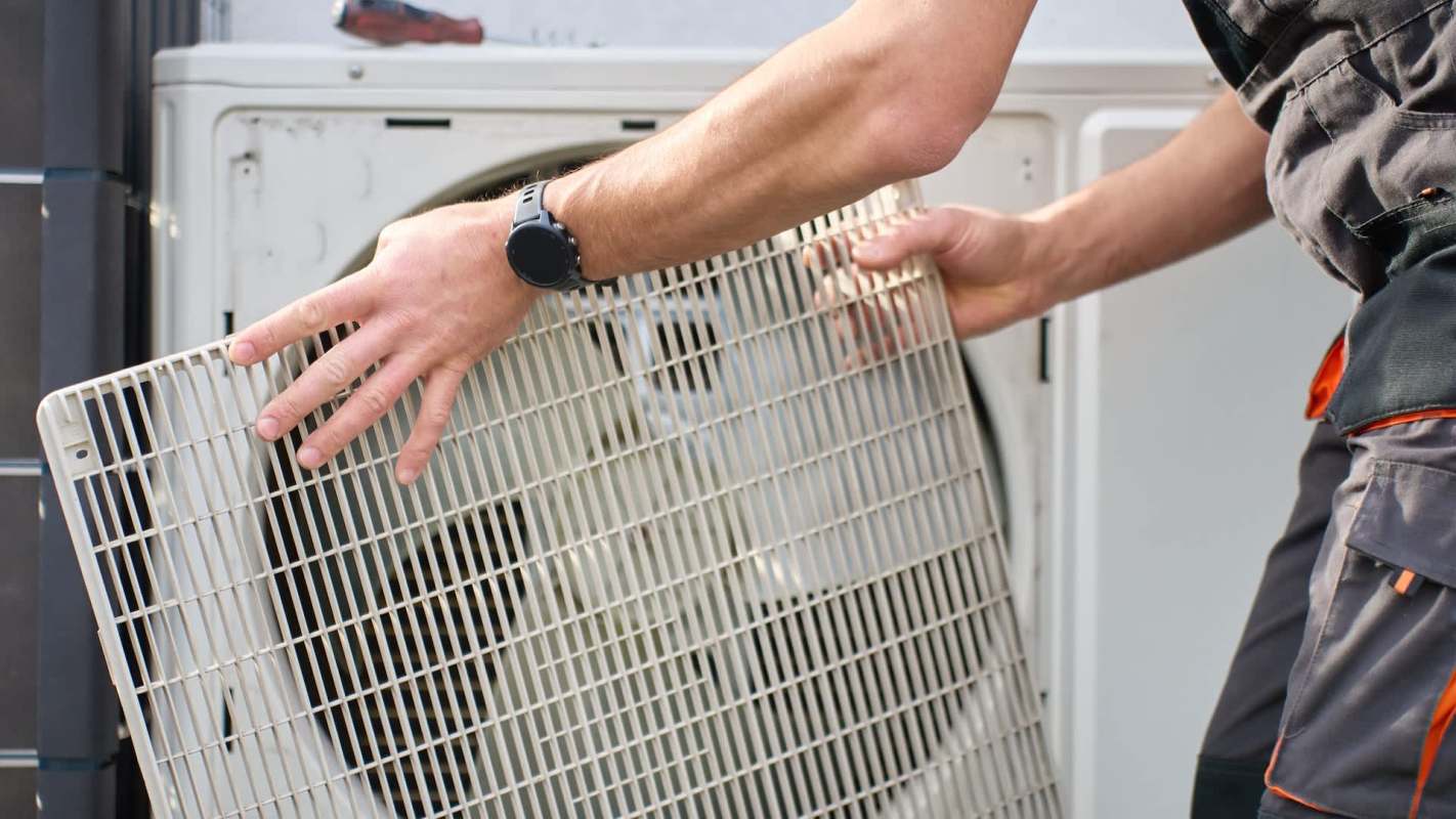 A person removes a filter from an outdoor air conditioning unit.