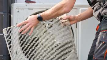 A person removes a filter from an outdoor air conditioning unit.