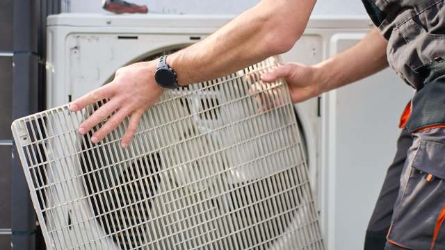 A person removes a filter from an outdoor air conditioning unit.
