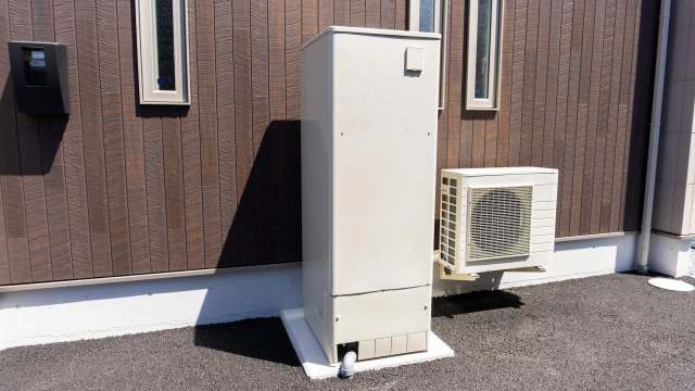 A white utility box and an air conditioning unit mounted on a brown wooden wall.