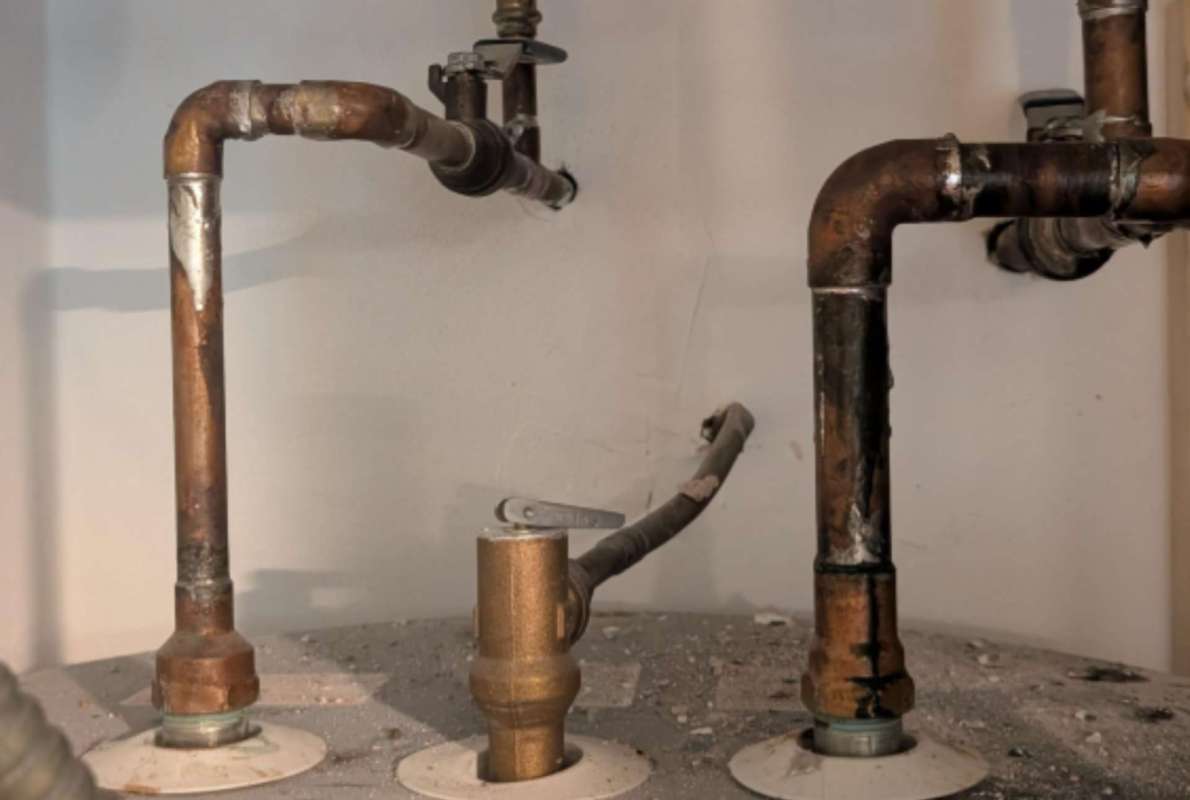Pipes and valves connected to a water heater, with some debris on the surface below.