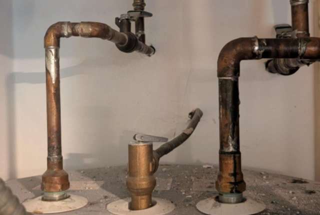 Pipes and valves connected to a water heater, with some debris on the surface below.