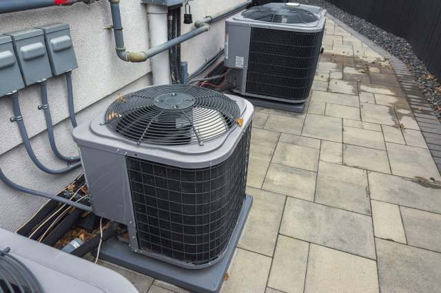 Air conditioning units positioned on a paved surface next to a building wall with electrical connections.