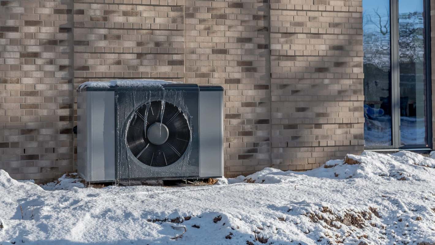 An outdoor heat pump surrounded by snow.