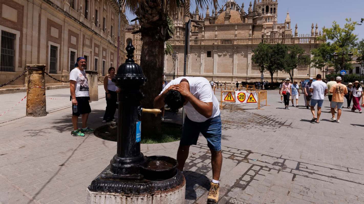 A person rinses their hair at a public fountain in a busy plaza.