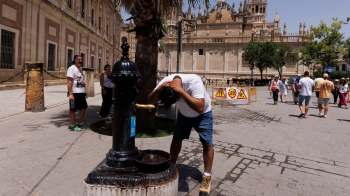 A person rinses their hair at a public fountain in a busy plaza.