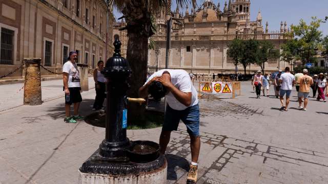 A person rinses their hair at a public fountain in a busy plaza.