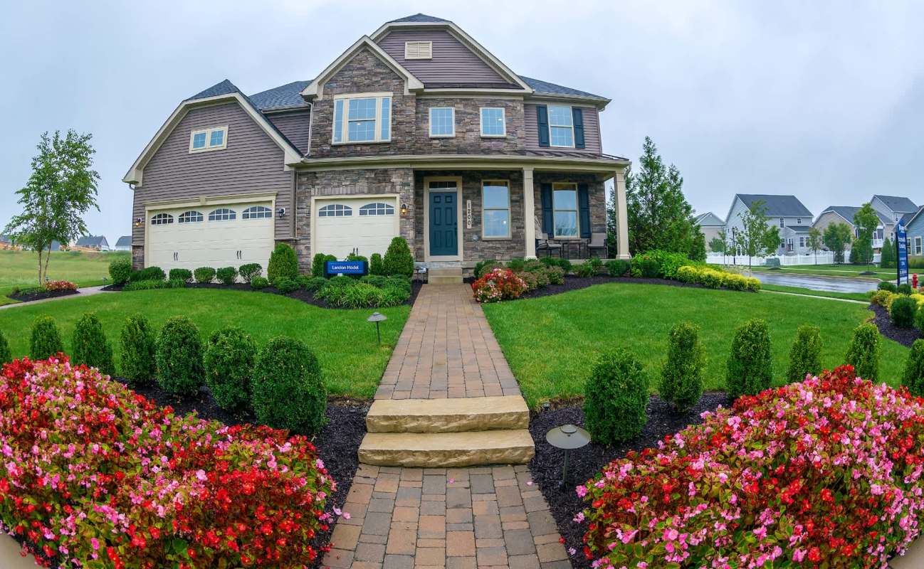A large house with a stone facade, surrounded by a well-manicured lawn and colorful flower beds.