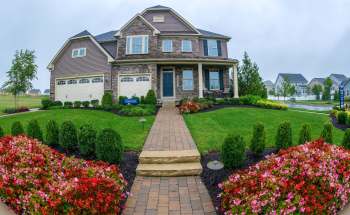 A large house with a stone facade, surrounded by a well-manicured lawn and colorful flower beds.