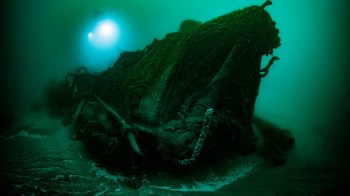 A submerged shipwreck covered in marine growth in dark, murky water.