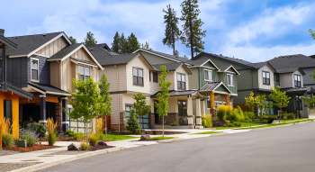 A row of modern houses with trees and landscaping along a residential street.