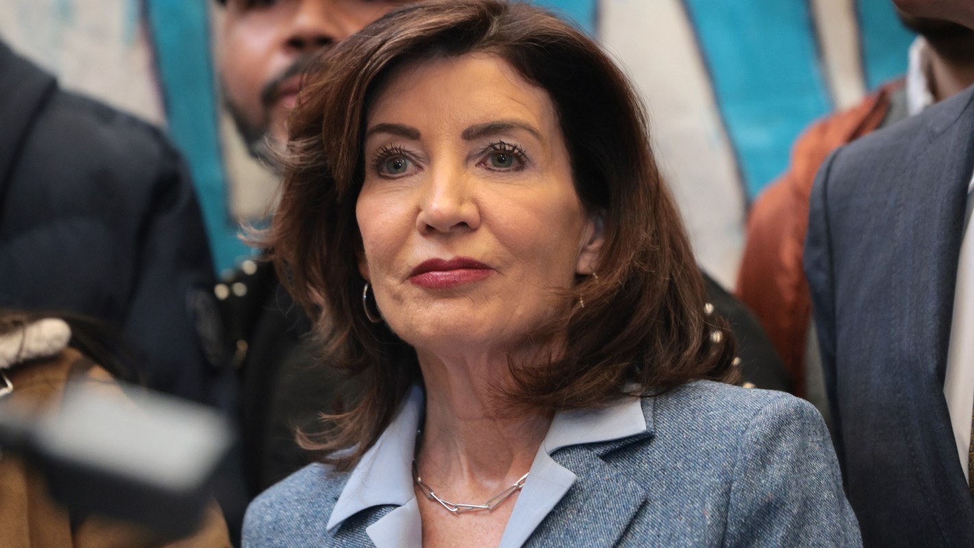 A woman wearing a blazer stands among a group of people in an indoor setting.