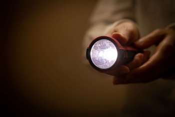 A person holds a flashlight emitting light in a dimly lit environment.
