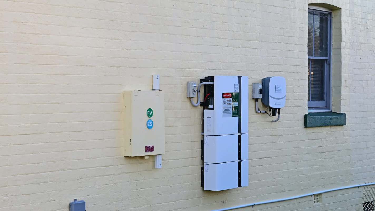Electrical equipment and inverters mounted on a yellow brick wall beside a window.