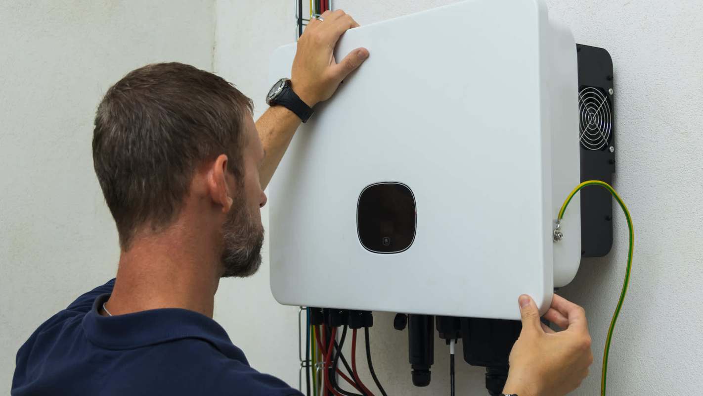 A person adjusts a white electrical unit mounted on a wall, with colorful wires visible.